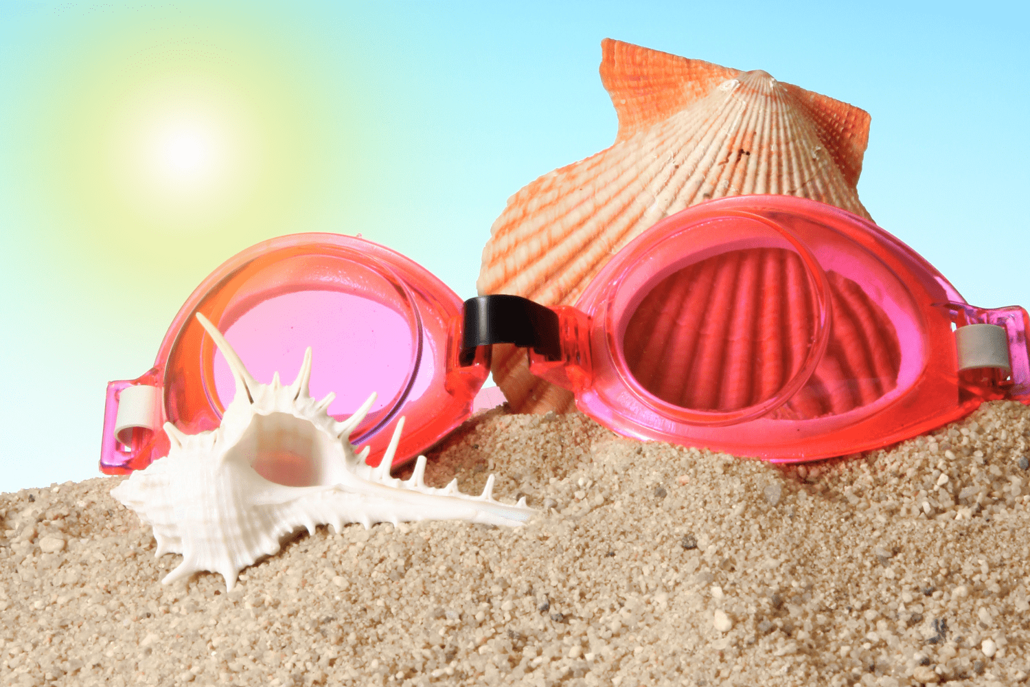 swimming googles with sea shells on sand